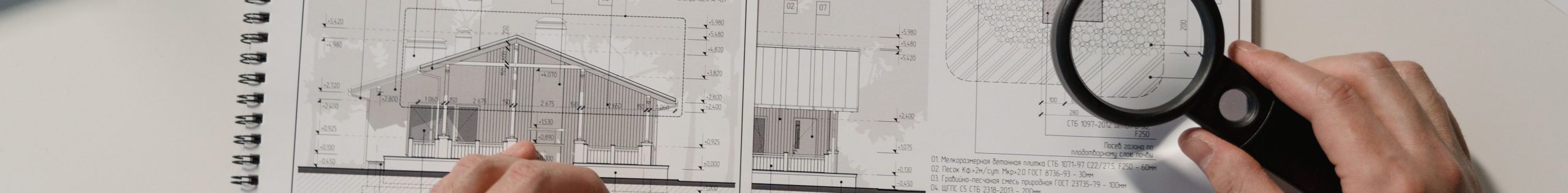 Hands holding a ruler and magnifying glass over architectural floor plans on a white table.
