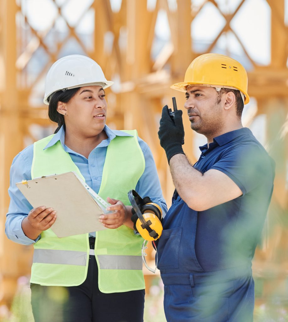 Engineers in safety gear discussing a construction project outdoors with visible scaffolding.